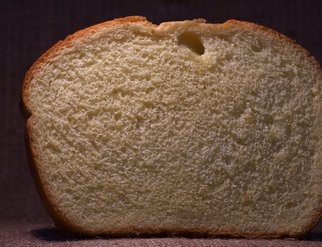 A slice of sandwich bread displayed on a brown background, highlighting its texture and color